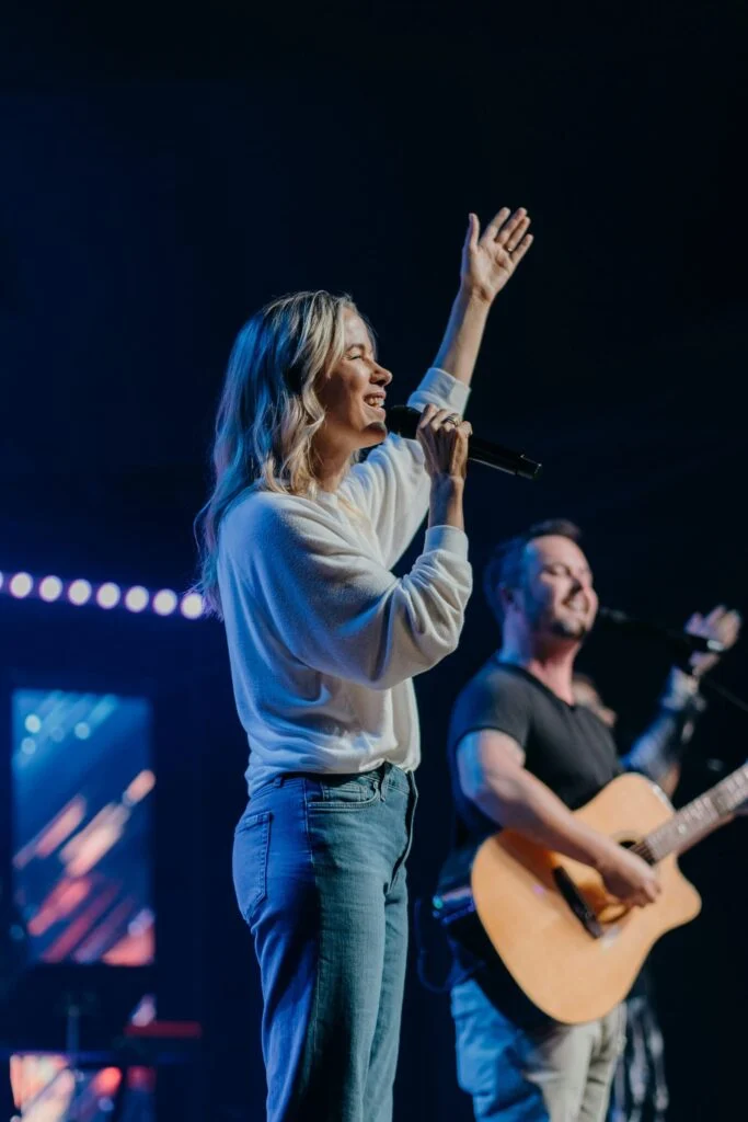A worship leader singing with one hand raised beside a guitarist
