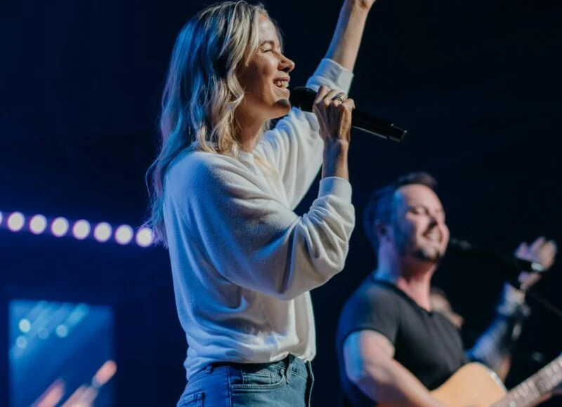 A worship leader singing with one hand raised beside a guitarist