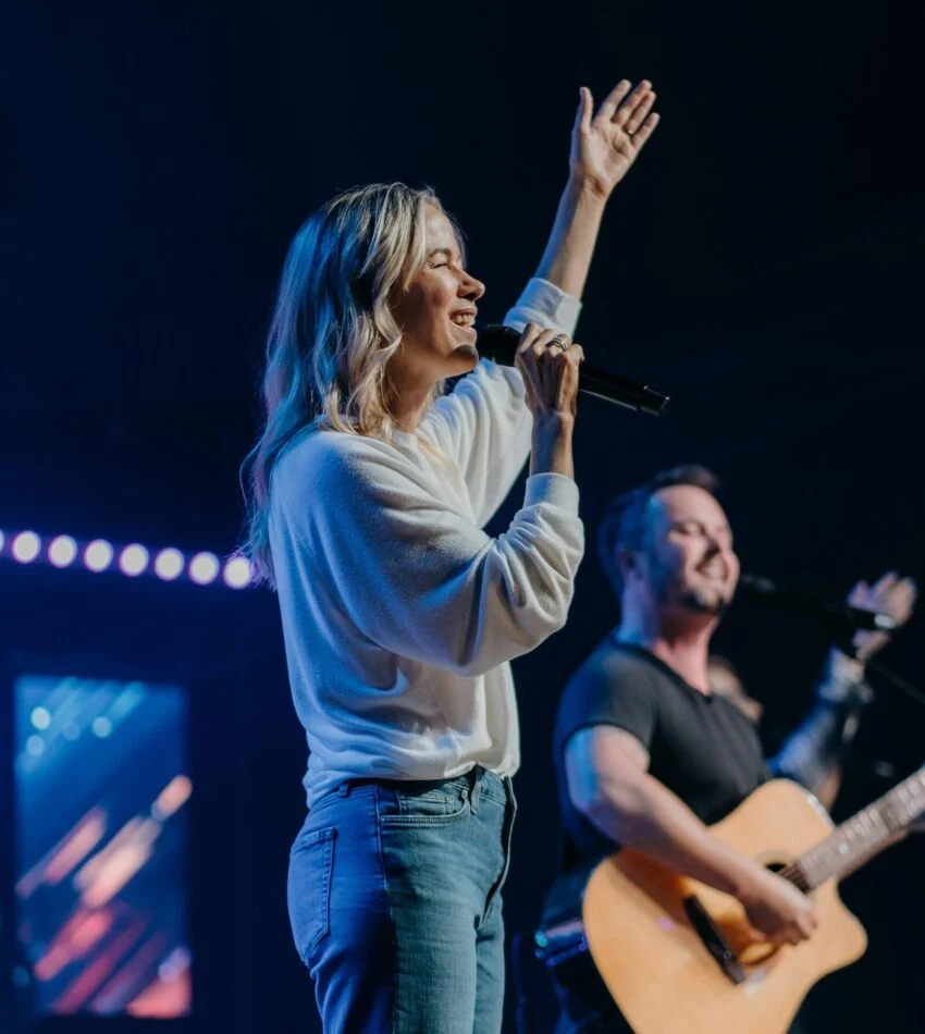 A worship leader singing with one hand raised beside a guitarist